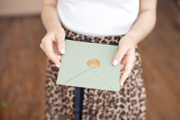 Close-up photo of female hands holding a silver blue or pink invitation envelope with a wax seal, a gift certificate, a postcard, a wedding invitation card