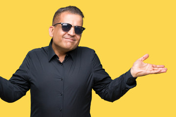 Middle age arab man wearing sunglasses over isolated background clueless and confused expression...