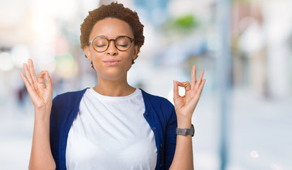 Young beautiful african american woman wearing glasses over isolated background relax and smiling with eyes closed doing meditation gesture with fingers. Yoga concept.