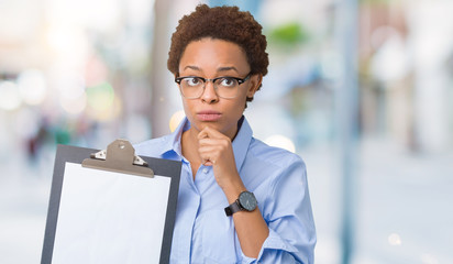 Young african american businesss woman holding clipboard over isolated background serious face...