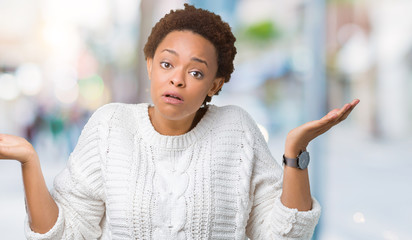 Beautiful young african american woman wearing sweater over isolated background clueless and confused expression with arms and hands raised. Doubt concept.