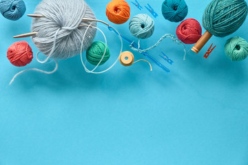 Various wool yarn, knitting needles and stuffed heart on mint colored paper background