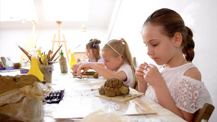 Children are sculpting toys from wet clay. They are using special tools under the guidance of a...