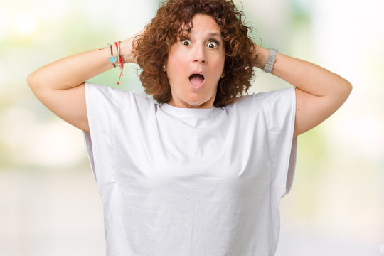 Beautiful middle ager senior woman wearing white t-shirt over isolated background Crazy and scared with hands on head, afraid and surprised of shock with open mouth