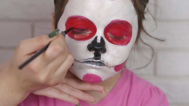Kid draws face for Halloween. An adorable little girl gets her face painted with paints. Body painting on the face of a child.