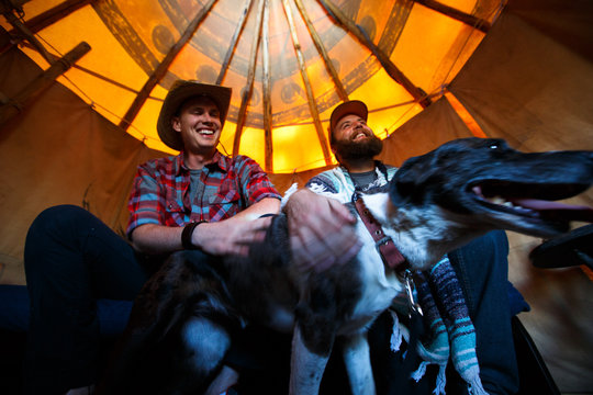 Two men laugh while petting a dog inside a tepee  in northeast Oregon at sunset.