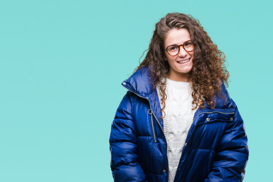 Beautiful young brunette curly hair girl wearing winter coat, glasses and sweater over isolated background with a happy and cool smile on face. Lucky person.