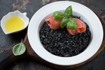 Risotto with squid-ink, salmon fillet, olive oil and fresh green basil