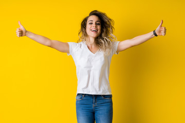 Beautiful young blonde woman jumping happy and excited with thumbs up over isolated yellow...