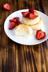 Cheese pancakes and  strawberries on the white plate  on the brown wooden background.Vertical location.Copy space.