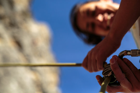A woman smiles before belaying a rock climber with an autolocking belay device.