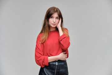 Photo portrait of a beautiful pretty brunette girl in a red sweater on a gray background. A woman is satisfied with her life, she stands in front of the camera, smiling and talking. Made in a studio.