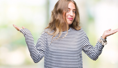 Beautiful young blonde woman wearing stripes sweater over isolated background clueless and confused expression with arms and hands raised. Doubt concept.