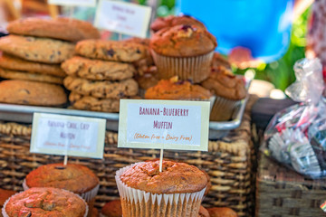 This is a color photo of homemade banana-blueberry gluten free and dairy free muffins. They have a descriptive sign on the muffins.