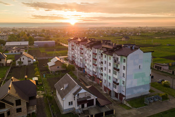 Fototapeta premium Top view of developing city landscape. Apartment building and suburb house roofs on pink sky at sunrise background. Drone photography.