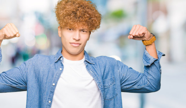 Young handsome man with afro hair wearing denim jacket showing arms muscles smiling proud. Fitness concept.