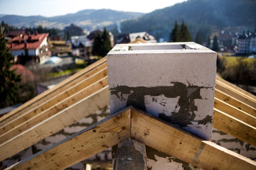 Close-up detail of roof frame of rough wooden lumber beams and chimney made of foam insulation blocks on blurred green background. Building, roofing, construction and renovation concept.