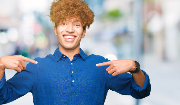 Young handsome elegant man with afro hair looking confident with smile on face, pointing oneself with fingers proud and happy.