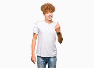 Young handsome man with afro hair wearing casual white t-shirt Beckoning come here gesture with hand inviting happy and smiling