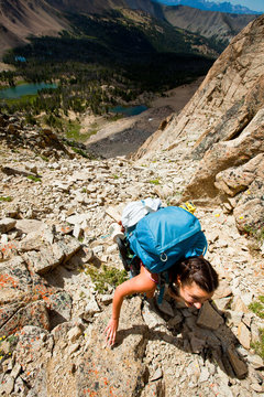 A woman makes the exposed, hairy scramble over the chossy Devil's Staircase, a shortcut to get from Born Lakes (in the background) to the Boulder Chain Lakes on the otherside of the pass in the White Cloud Mountains in Idaho.