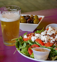 A salad with tomatoes, pecans and feta cheese on a plate and served with a beer.