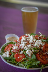 A salad with tomatoes, pecans and feta cheese on a plate and served with a beer.