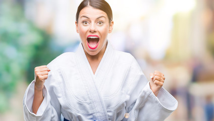 Young beautiful woman wearing karate kimono uniform over isolated background celebrating surprised and amazed for success with arms raised and open eyes. Winner concept.