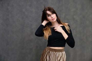Photo portrait of a beautiful pretty brunette girl in a black sweater on a gray background. A woman is satisfied with her life, she stands in front of the camera, smiling and talking. Made in studio.