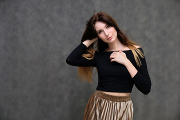 Photo portrait of a beautiful pretty brunette girl in a black sweater on a gray background. A woman is satisfied with her life, she stands in front of the camera, smiling and talking. Made in studio.