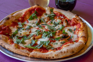 This is a color photo of a whole spinach, garlic and cheese pizza, freshly cooked on a metal serving dish.