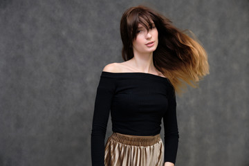 Photo portrait of a beautiful pretty brunette girl in a black sweater on a gray background. A woman is satisfied with her life, she stands in front of the camera, smiling and talking. Made in studio.