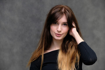 Beauty portrait of a beautiful pretty brunette girl in a black sweater on a dark gray background. A woman is happy with life, she is standing in front of the camera, smiling. Made in a studio.