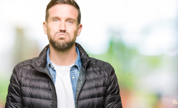 Handsome man wearing winter coat puffing cheeks with funny face. Mouth inflated with air, crazy expression.