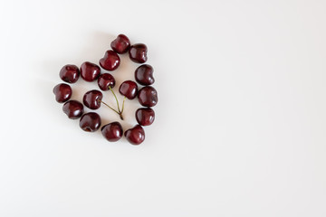 Heart made of red sweet  cherries near a cup with a sweet cherries on a white background.  Top view. Copy space.