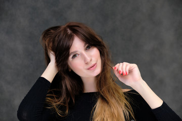 Fototapeta premium Beauty portrait of a beautiful pretty brunette girl in a black sweater on a dark gray background. A woman is happy with life, she is standing in front of the camera, smiling. Made in a studio.