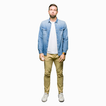 Handsome man with blue eyes and beard wearing denim jacket puffing cheeks with funny face. Mouth inflated with air, crazy expression.