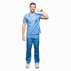 Fototapeta premium Handsome doctor man wearing medical uniform over isolated background Pointing with hand finger to face and nose, smiling cheerful