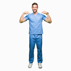 Fototapeta premium Handsome doctor man wearing medical uniform over isolated background looking confident with smile on face, pointing oneself with fingers proud and happy.