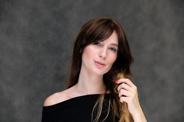 Beauty portrait of a beautiful pretty brunette girl in a black sweater on a dark gray background. A woman is happy with life, she is standing in front of the camera, smiling. Made in a studio.