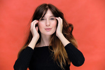 Beauty portrait of a beautiful pretty brunette girl in a black sweater on a red background. A woman is happy with life, she is standing in front of the camera, smiling. Made in a studio.