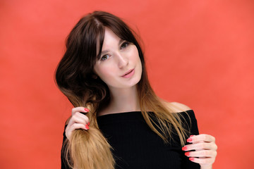Fototapeta premium Beauty portrait of a beautiful pretty brunette girl in a black sweater on a red background. A woman is happy with life, she is standing in front of the camera, smiling. Made in a studio.