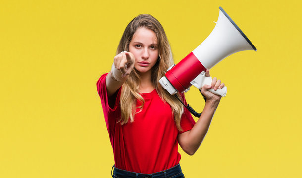 Young beautiful blonde woman yelling through megaphone over isolated background pointing with finger to the camera and to you, hand sign, positive and confident gesture from the front