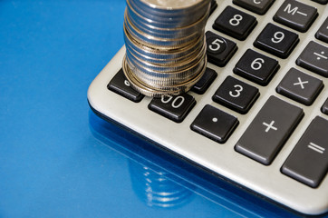 coins and calculator on blue background, reflecting