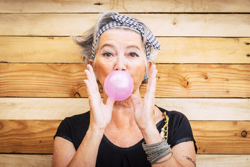 Funny and alternative old people caucasian beautiful woman with pink bubble chewing gum - portrait...