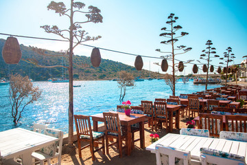 View of restaurant or cafe and bougainvillea flowers on beach in Gumusluk, Bodrum city of Turkey. Aegean seaside style colorful chairs, tables and flowers in Bodrum town near beautiful Aegean Sea.
