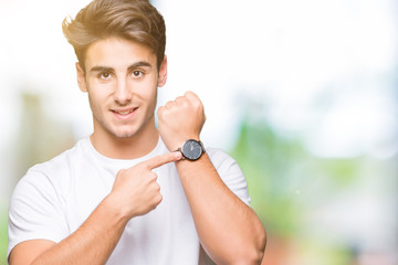 Young handsome man wearing white t-shirt over isolated background In hurry pointing to watch time,...
