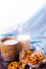 handmade ceramic cup. Coffee, pretzels and a bottle of milk on a blue textile background. Handmade tray with drops. Delicate serving. Cozy atmosphere. Handmade dishes in the interior.