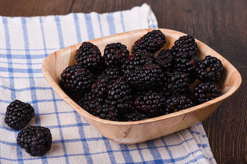 A few blackberries in a wooden bowl. Blackberry on a kitchen towel on a wooden table.
