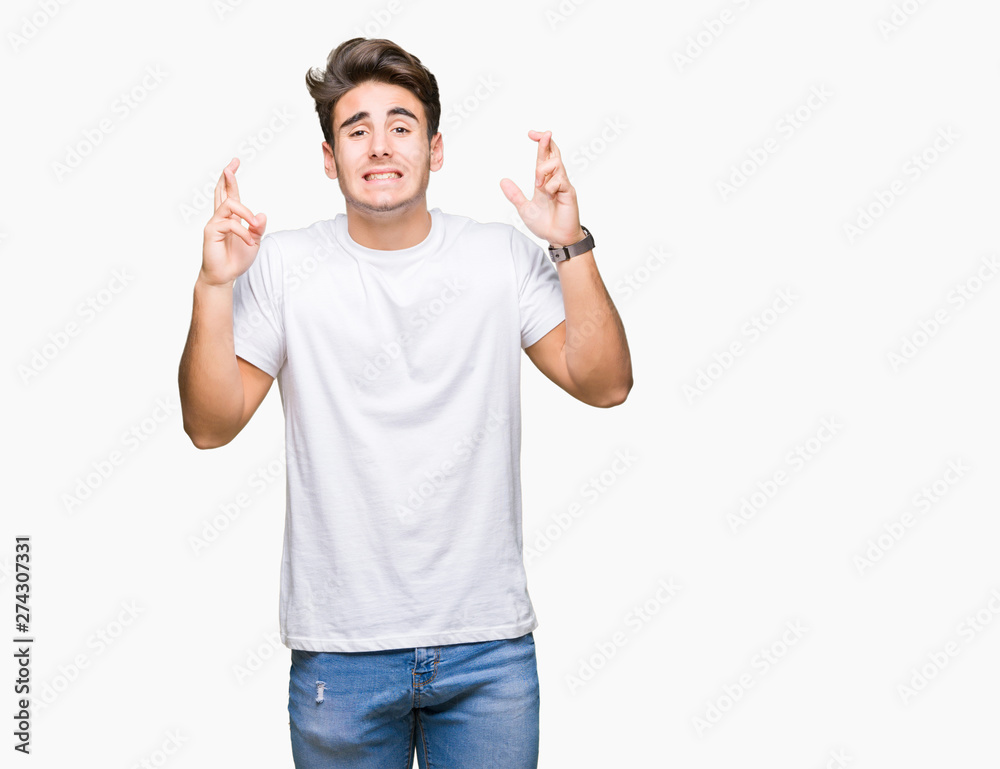 Wall mural young handsome man wearing white t-shirt over isolated background smiling crossing fingers with hope