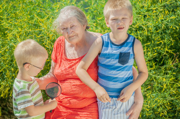 Portrait of elderly woman in red dress and hat with chidren. Pensioner maintains health and looks great on the background of the garden. Medical Chamomile flowers. Kids love granny